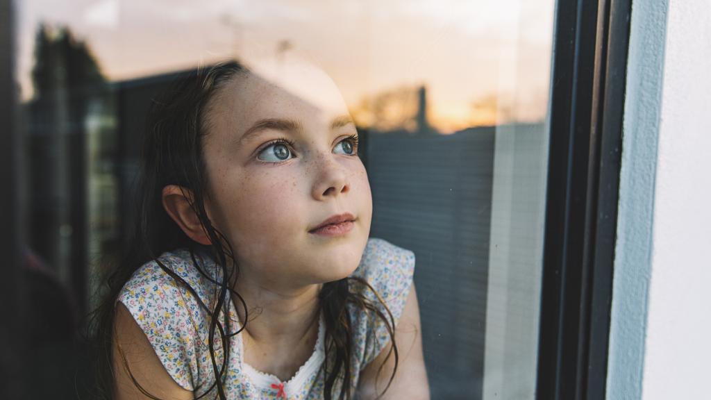 Young girl looking through window at sunset