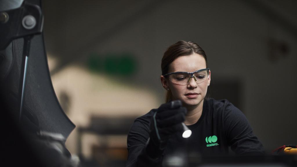 Female engineer wearing safety glasses while working under the hood of an Accelera-powered zero-emissions vehicle