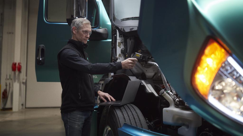 Male technician using a laptop to run diagnostics under the hood of a heavy-duty, zero-emission truck