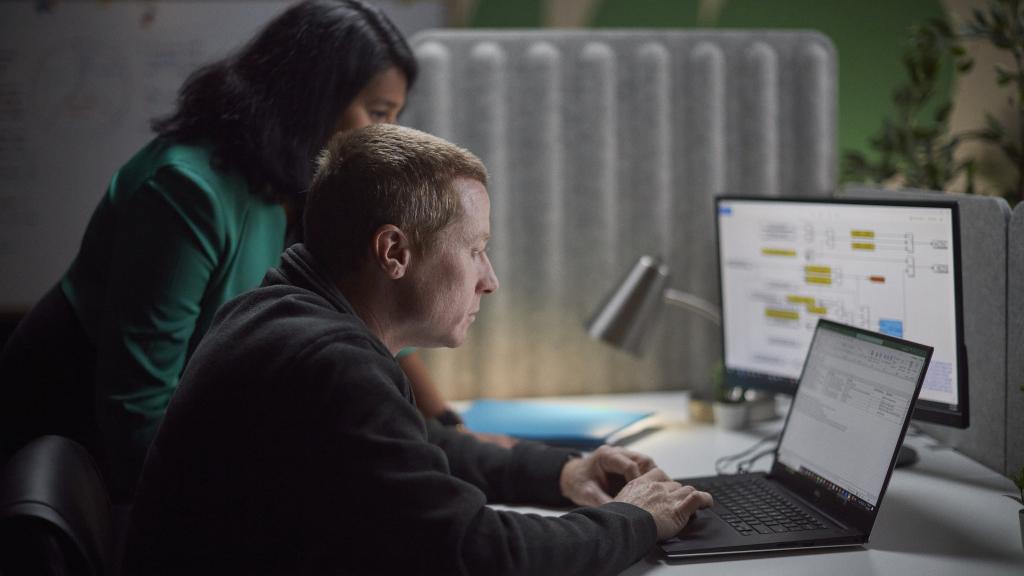 Two Accelera employees gathered around a desk, reviewing work on a laptop and secondary monitor