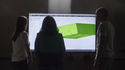Three engineers examining a 3D rendering on a tv screen