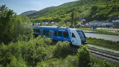 Blue passenger train powered by hydrogen running on train tracks past green foliage