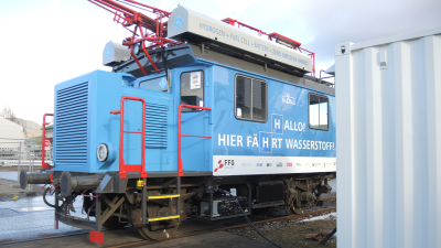 Locomotora de carga azul con barandillas rojas conectadas a un cargador eléctrico