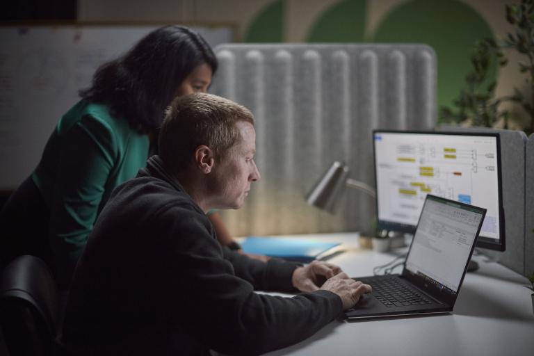 Two Accelera employees gathered around a desk, reviewing work on a laptop and secondary monitor