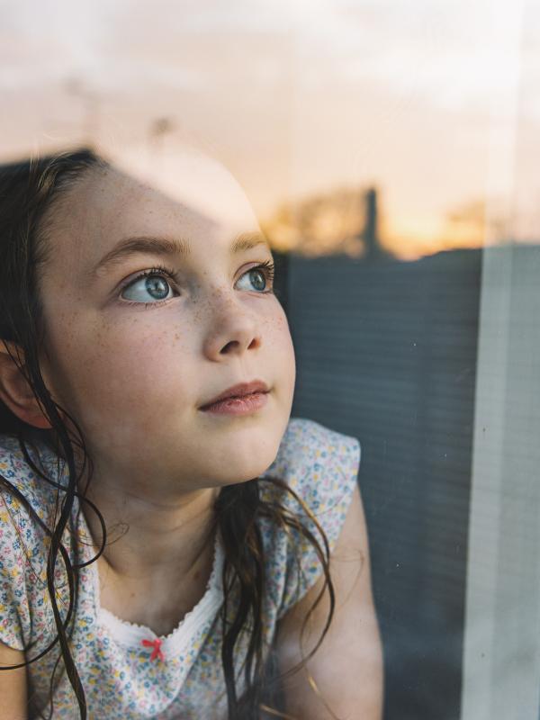 Young girl looking through window at sunset