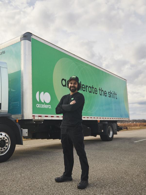 Truck diver with arms crossed standing in front of an electric truck powered by Accelera technology