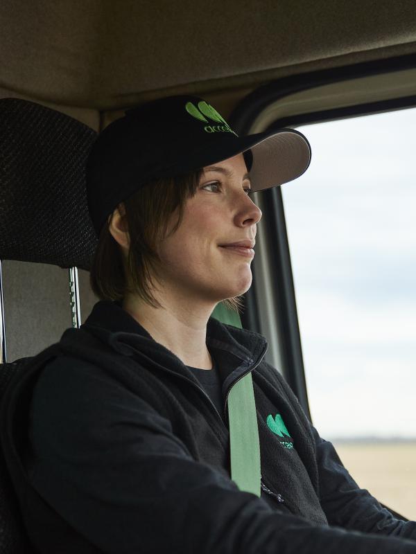 Close up image of a female truck driver with short hair, wearing an Accelera baseball hat, driving a zero-emission truck
