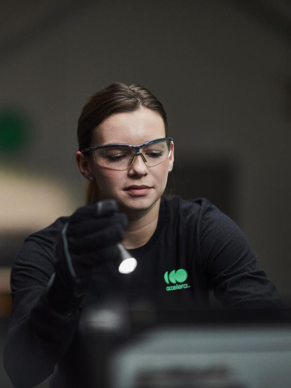Female engineer wearing safety glasses while working under the hood of an Accelera-powered zero-emissions vehicle