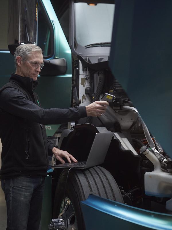 Male technician using a laptop to run diagnostics under the hood of a heavy-duty, zero-emission truck