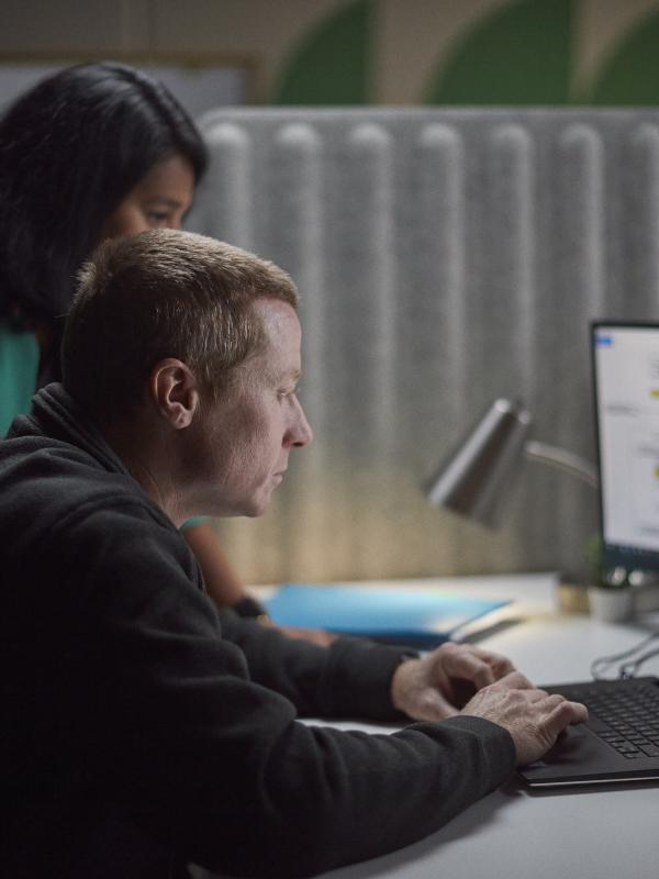 Two Accelera employees gathered around a desk, reviewing work on a laptop and secondary monitor