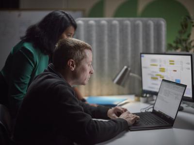 Dos empleados de Accelera reunidos alrededor de un escritorio, revisando el trabajo en una computadora portátil y un monitor secundario