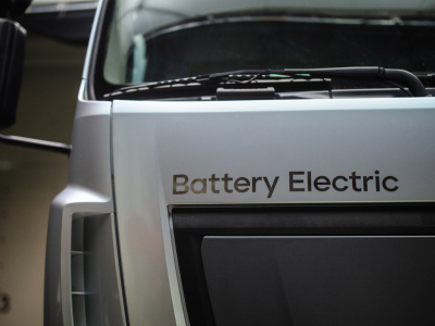 Front of a silver truck cab with the worlds "battery electric" above the grill plate.