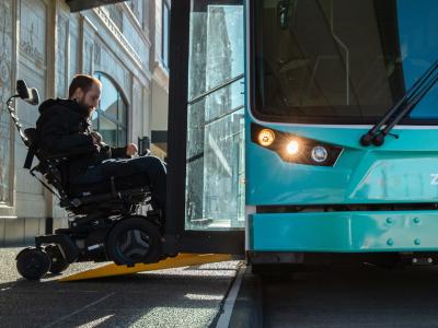 Person in motorized wheel chair using ramp to board a low-floor bus