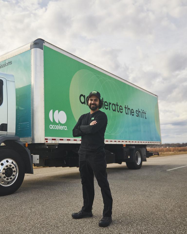 Truck diver with arms crossed standing in front of an electric truck powered by Accelera technology