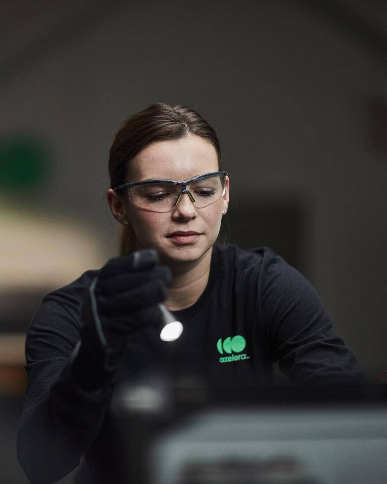 Ingeniera con gafas de seguridad mientras trabaja bajo el capó de un vehículo de cero emisiones impulsado por Accelera