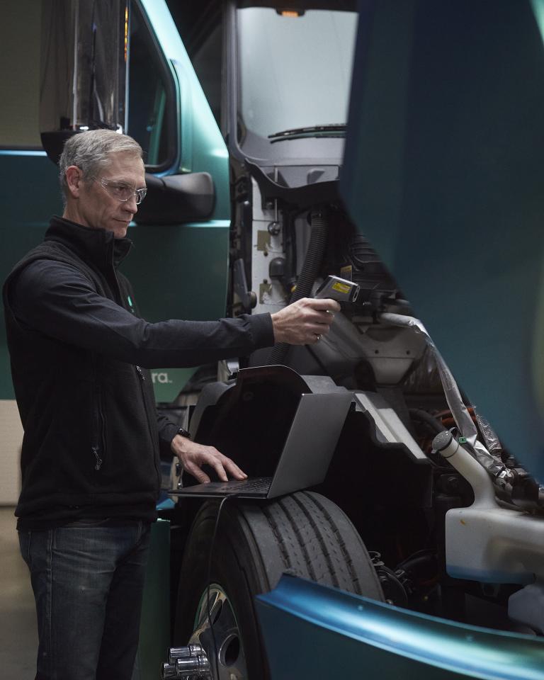 Male technician using a laptop to run diagnostics under the hood of a heavy-duty, zero-emission truck 