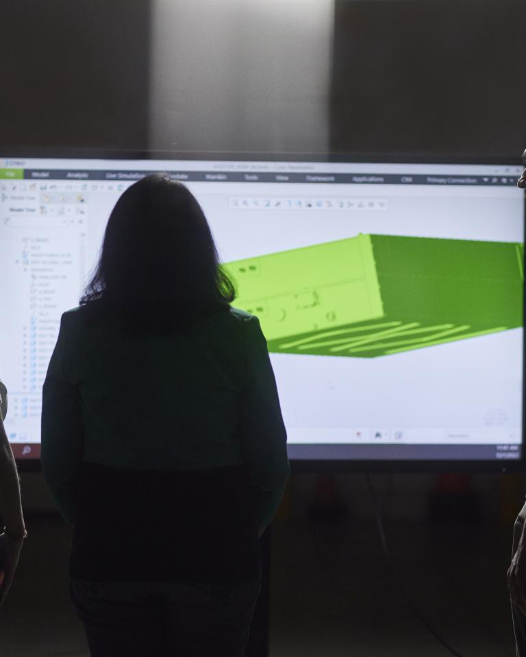 Three engineers examining a 3D rendering on a tv screen