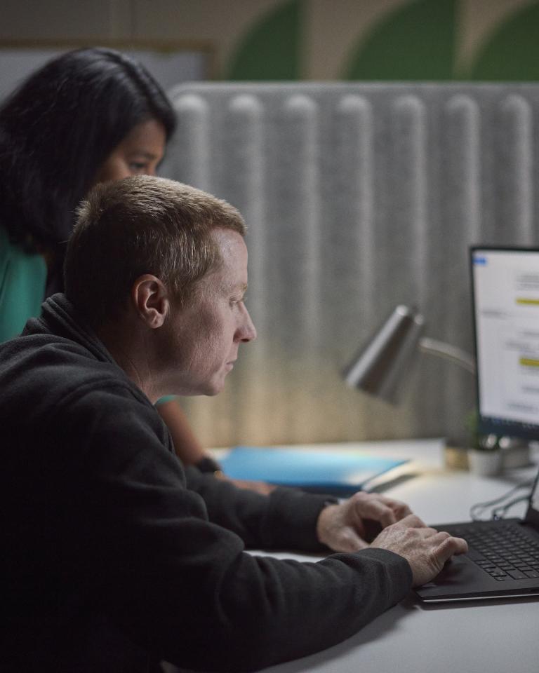 Two Accelera employees gathered around a desk, reviewing work on a laptop and secondary monitor
