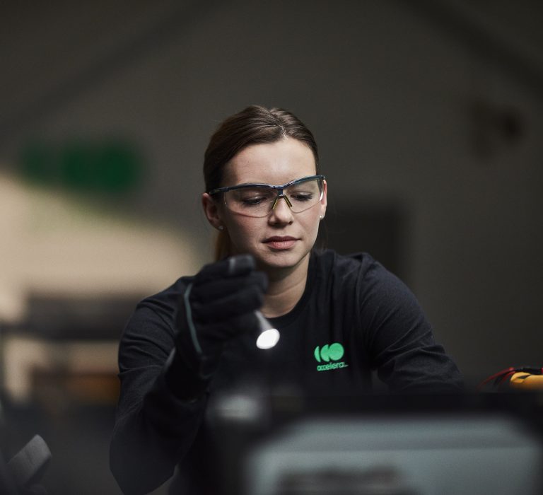 Female engineer wearing safety glasses while working under the hood of an Accelera-powered zero-emissions vehicle