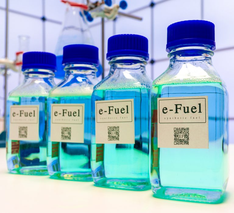 Four bottles with blue caps filled with blue liquid and labeled as e-Fuel