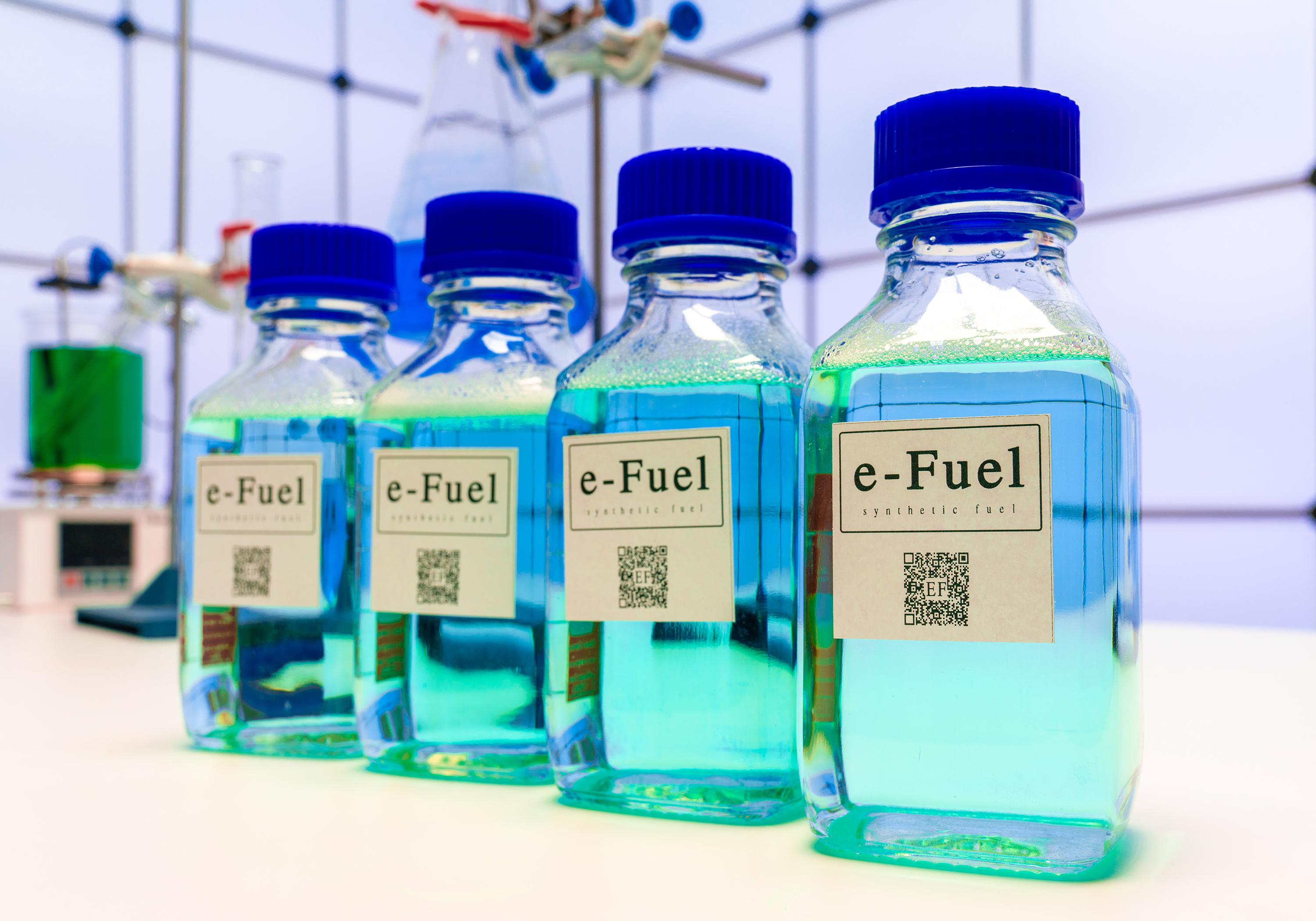 Four bottles with blue caps filled with blue liquid and labeled as e-Fuel
