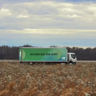 Accelera-Batterie-Elektrolastwagen, der an leeren Feldern vorbeifährt