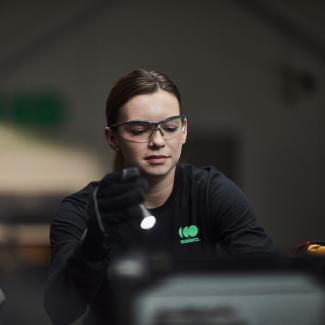 Female engineer wearing safety glasses while working under the hood of an Accelera-powered zero-emissions vehicle