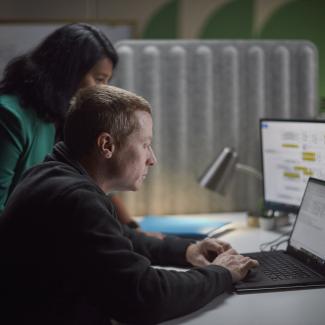 Two Accelera employees gathered around a desk, reviewing work on a laptop and secondary monitor