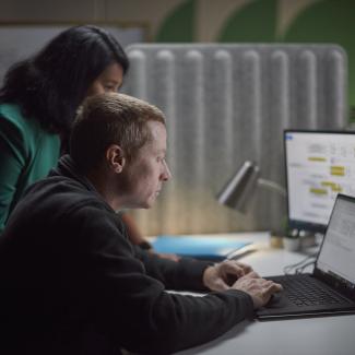 Dos empleados de Accelera reunidos alrededor de un escritorio, revisando el trabajo en una computadora portátil y un monitor secundario